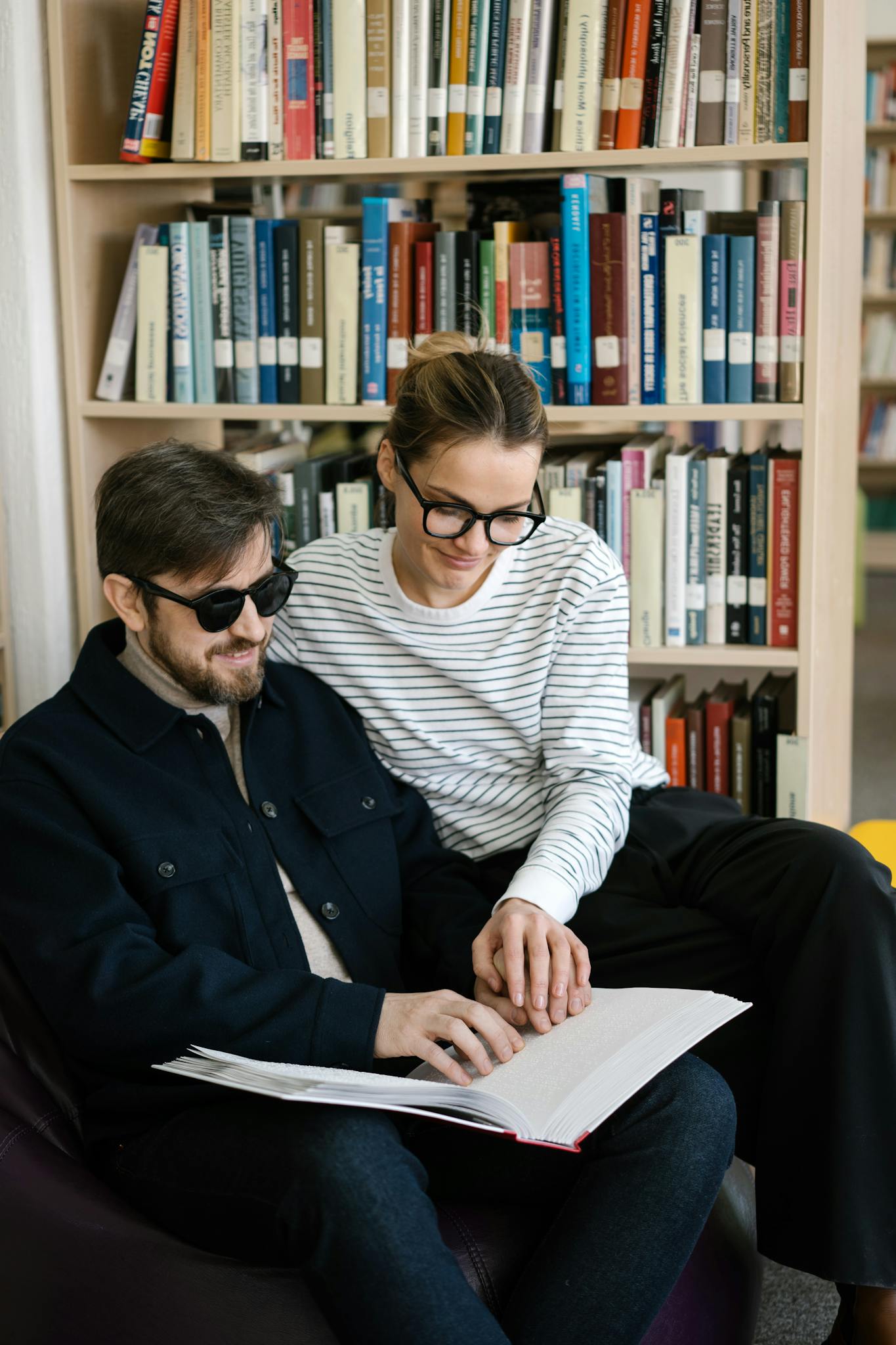 Man and woman reading a braille book in a library, emphasizing support and accessibility.